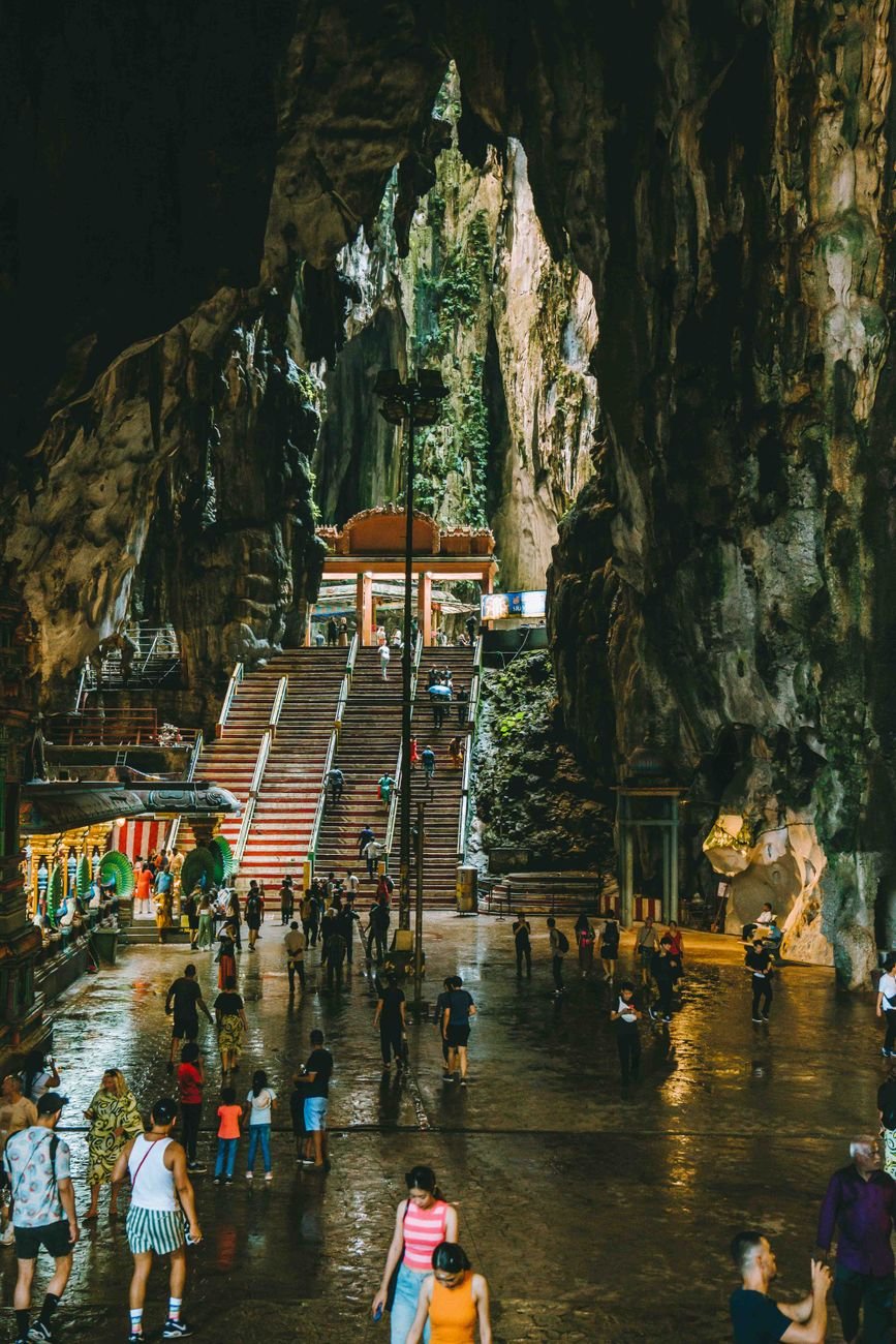 People descending a long stairway inside a cave, lit by daylight from above.
