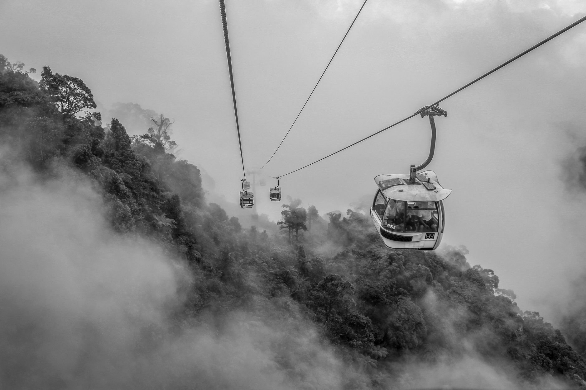Cable cars strung between hillside towers, seen through mist.
