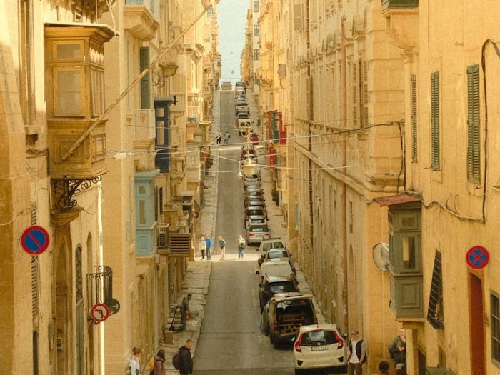 A steep, narrow street lined with sandstone buildings and wooden balconies, with a cathedral dome in the distance.