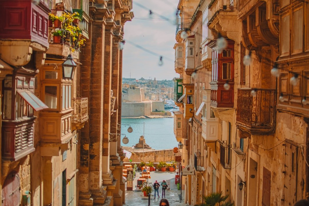 Traditional wooden balconies framing a narrow stone street that opens onto a fortified harbour.