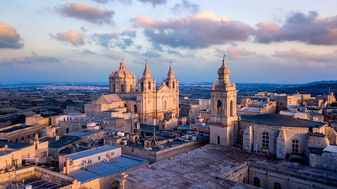 Twin bell towers and a stone dome catching evening light above a hilltop old town.