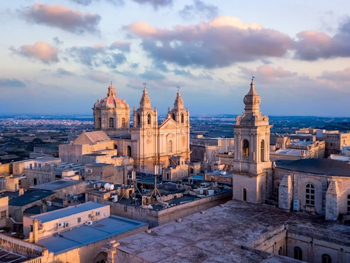 Twin bell towers and a stone dome catching evening light above a hilltop old town.