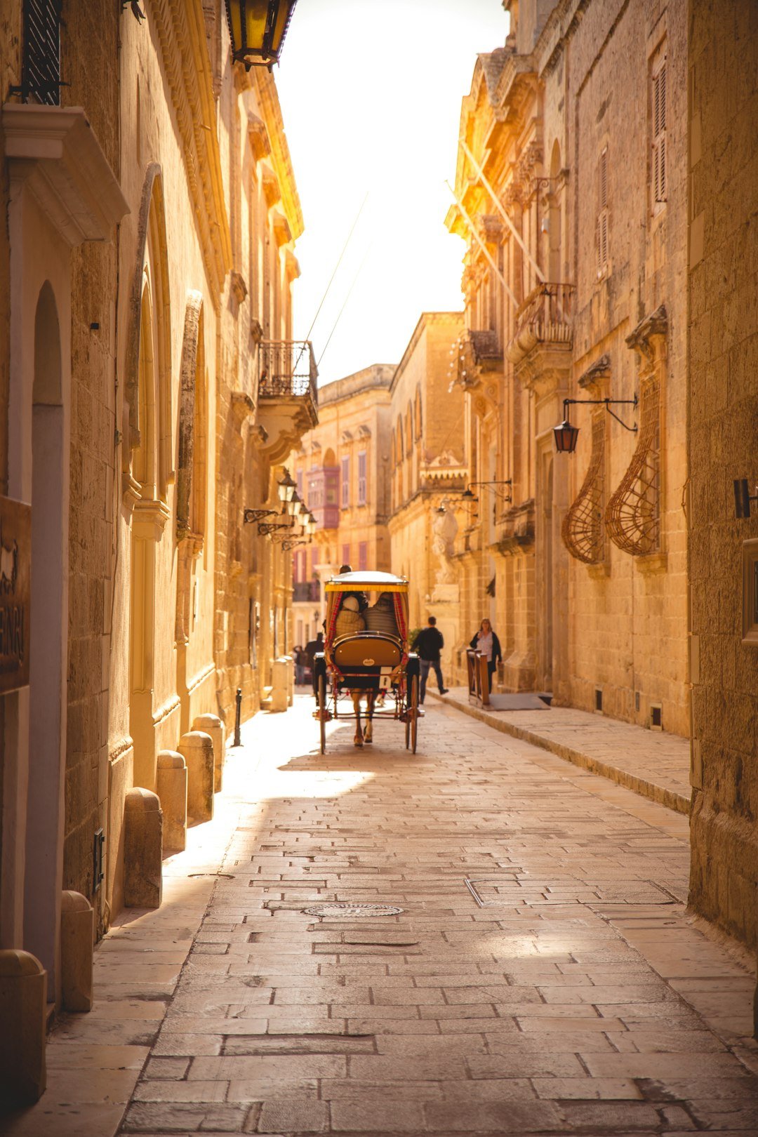 A horse-drawn carriage moving down a narrow sandstone street lined with old buildings.