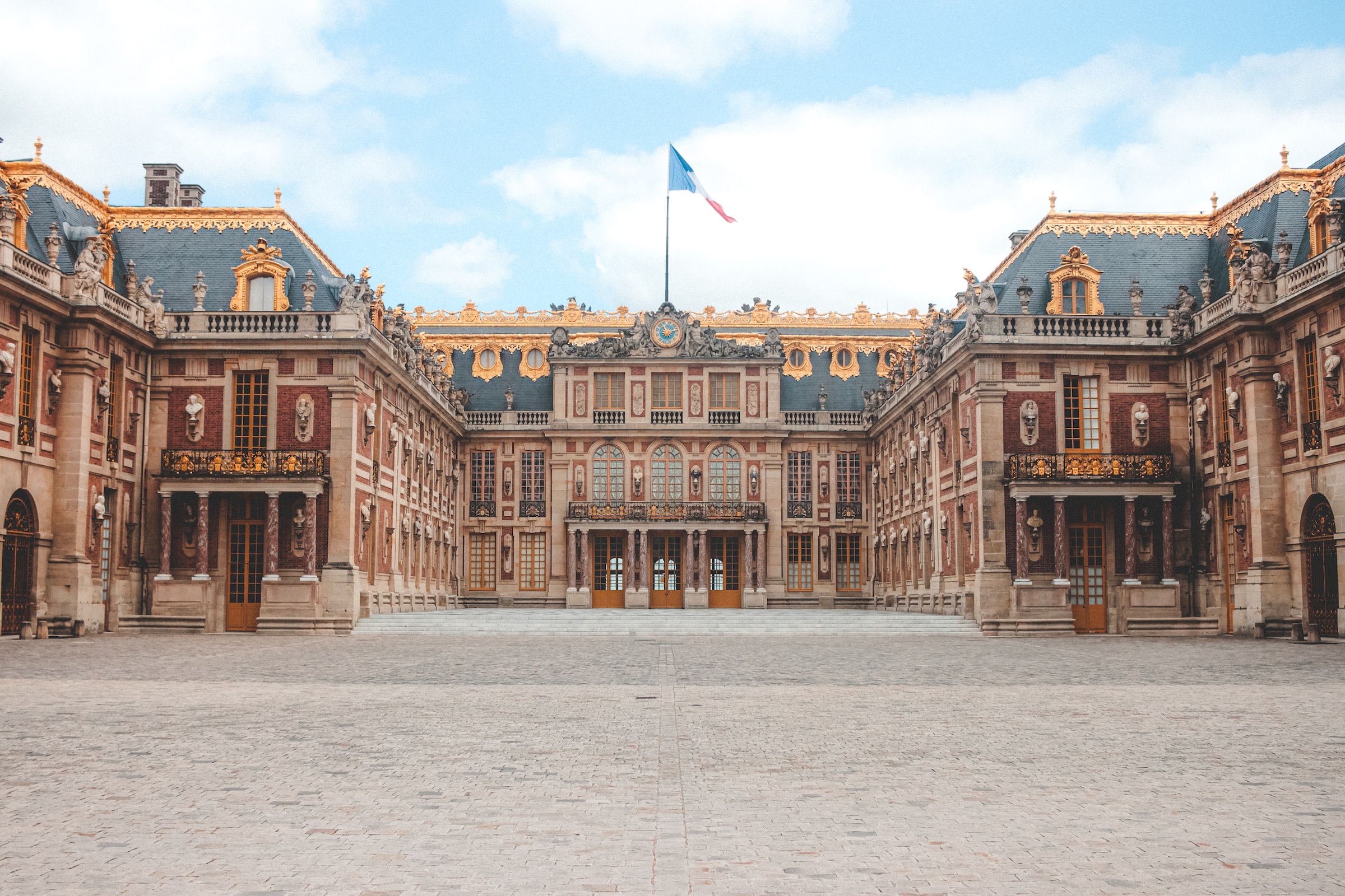 Palace of Versailles courtyard with a French flag atop the central roofline