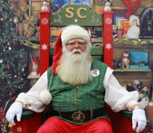 Santa Claus sits in a chair looking at the camera.