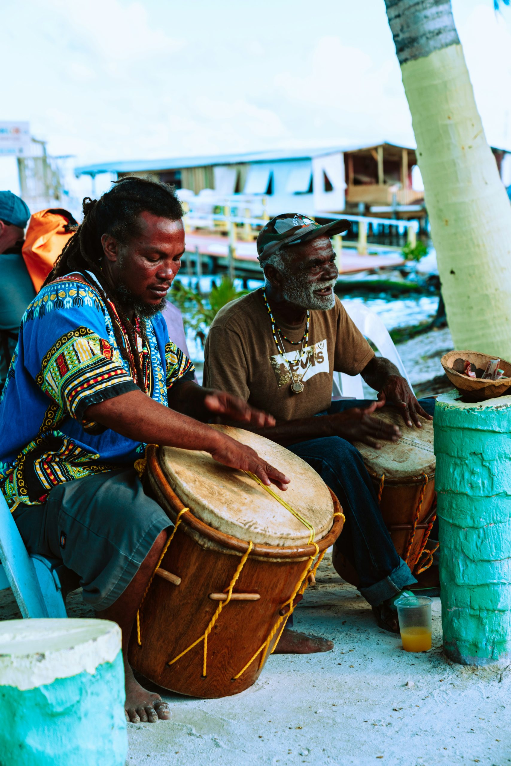 Musicians play traditional drums beside a palm tree near the water