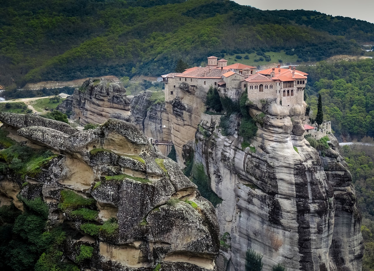 A monastery perches atop tall rock pillars in Meteora, surrounded by forested hills