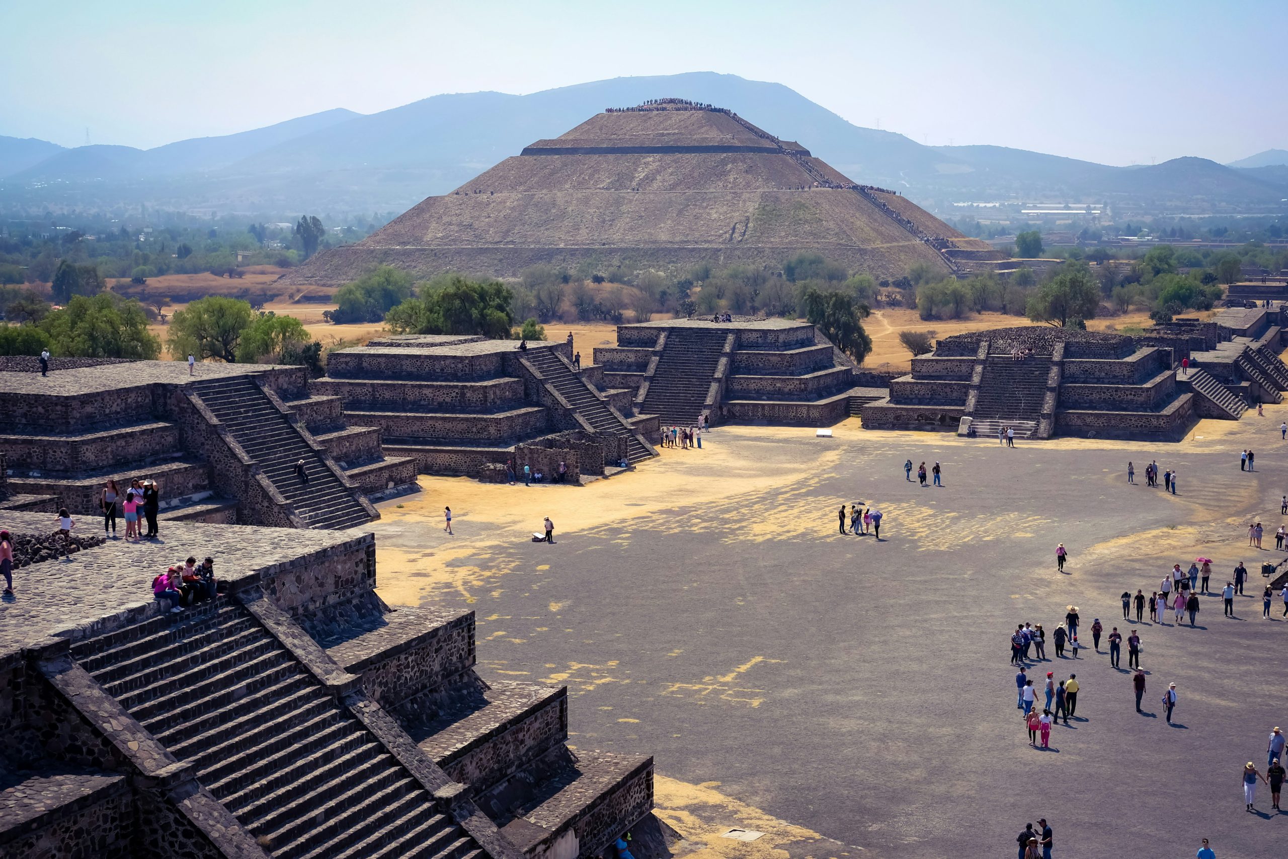 The Pyramid of the Sun seen along the Avenue of the Dead, with smaller stepped platforms in the foreground and hills behind.