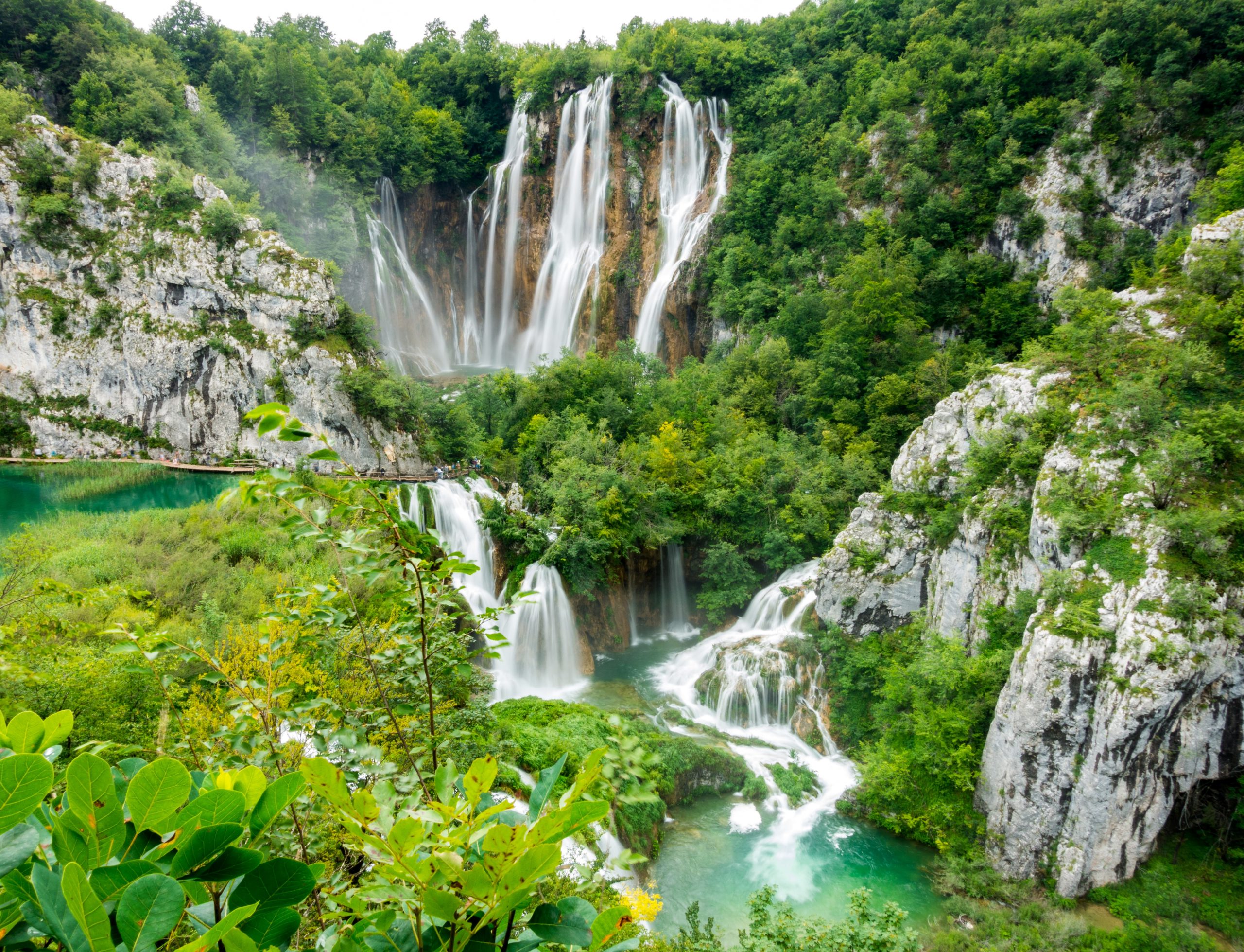 Teen travelers pause among tiered limestone cliffs as waterfalls cascade into turquoise pools at Plitvice Lakes