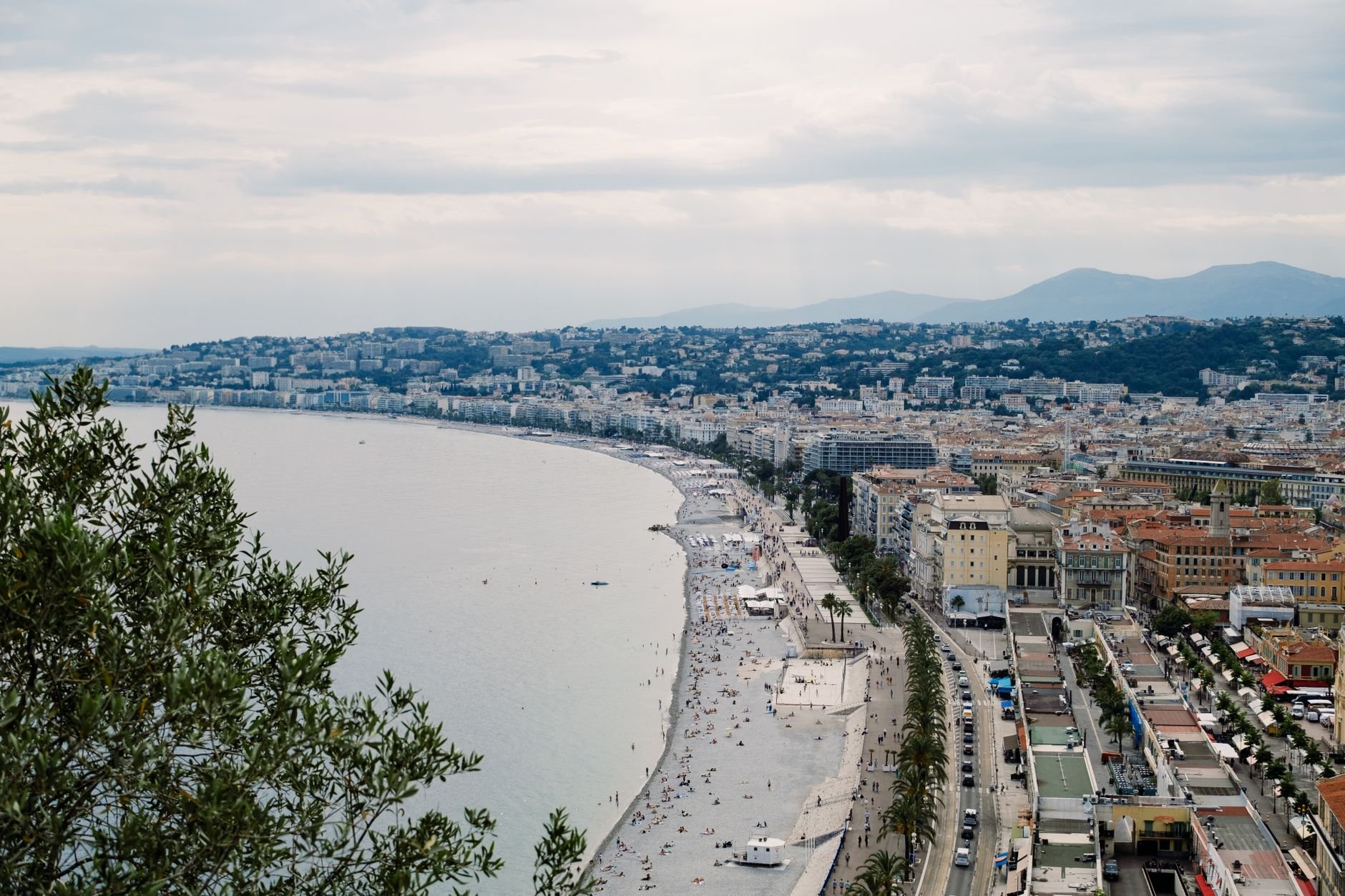 A panoramic coastline of a city curving along the sea beneath green hills.