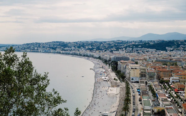 A panoramic coastline of a city curving along the sea beneath green hills.