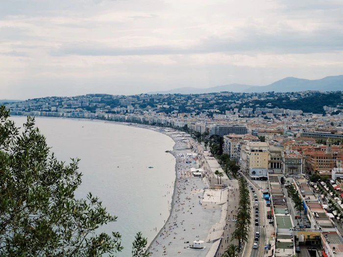 A panoramic coastline of a city curving along the sea beneath green hills.