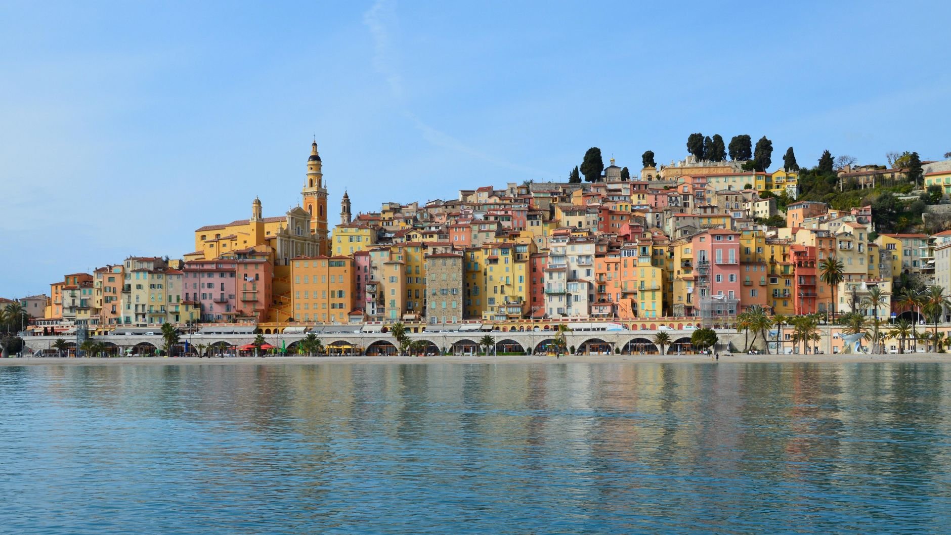 A town built along a curved sea shore beneath green hills.