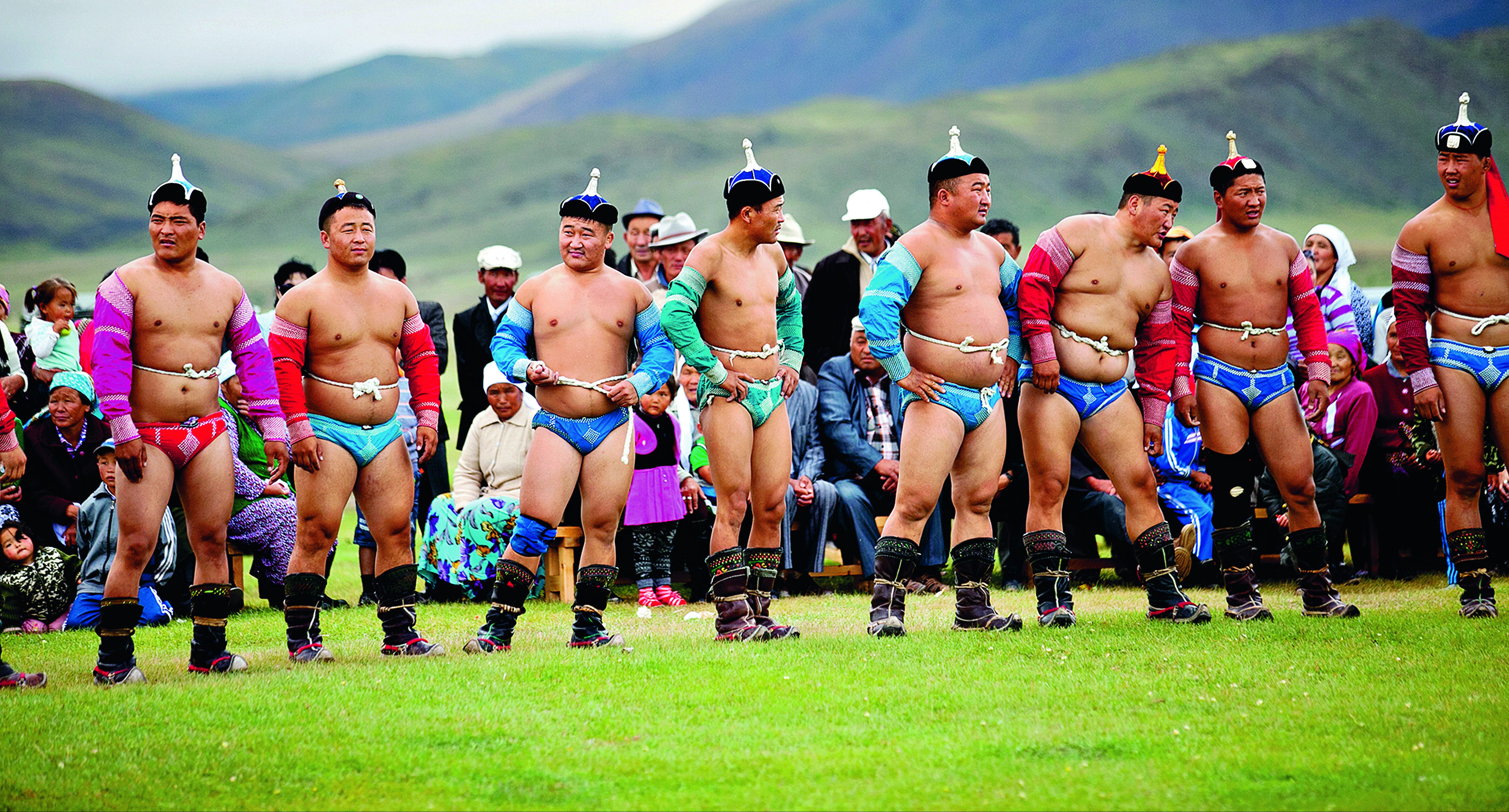 On this school trip, traditional wrestlers in ceremonial costume perform an eagle-style entrance dance before a crowd on the grass