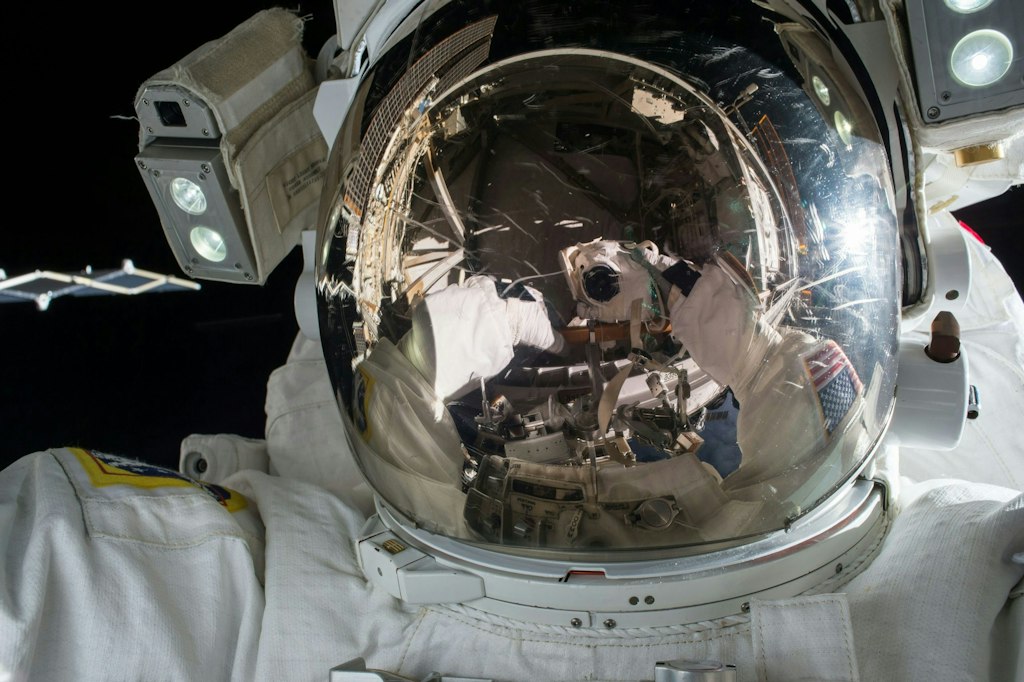 A scene is reflected in the helmet of an astronaut.