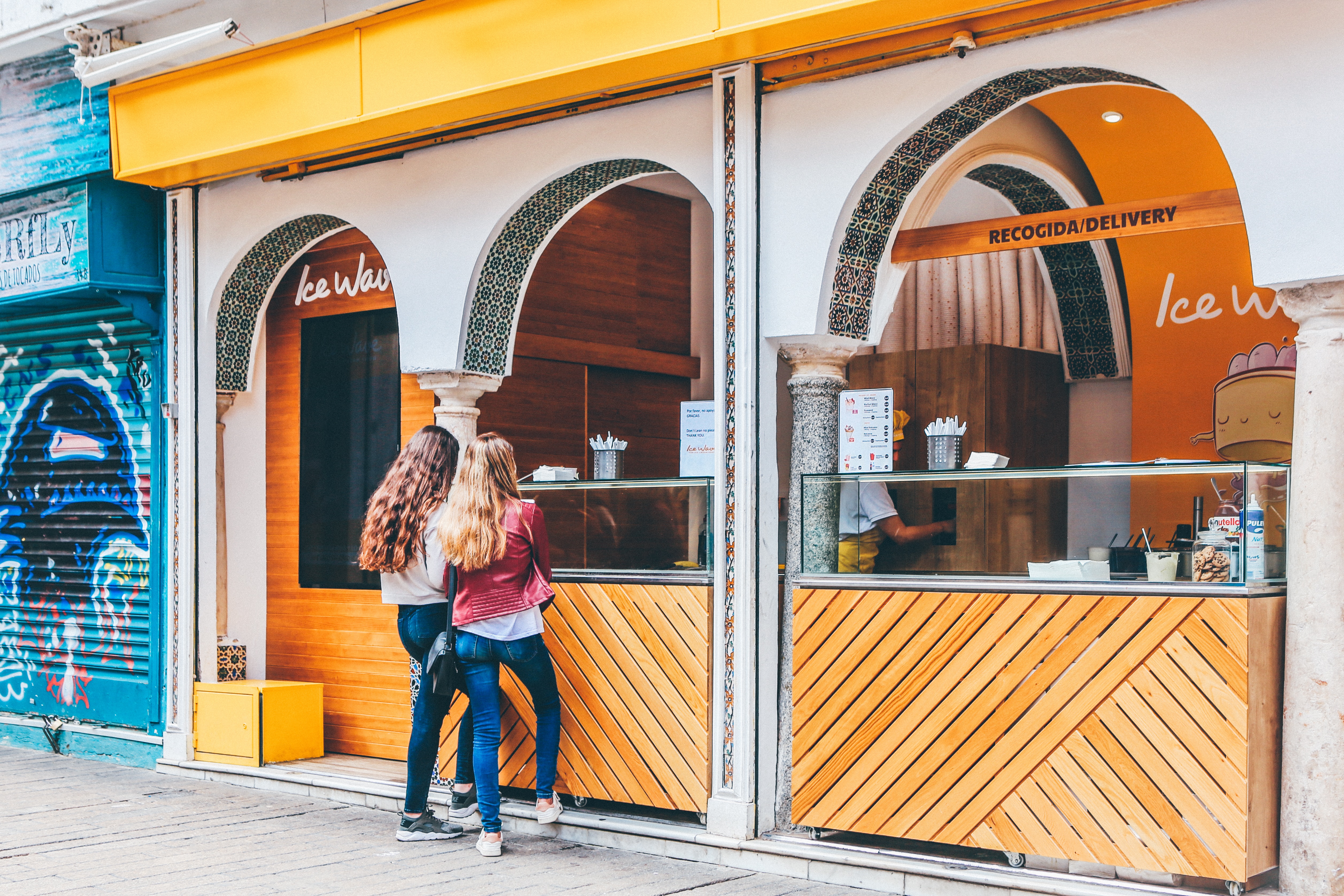 Students order at an ice cream shop window with arched wooden storefronts