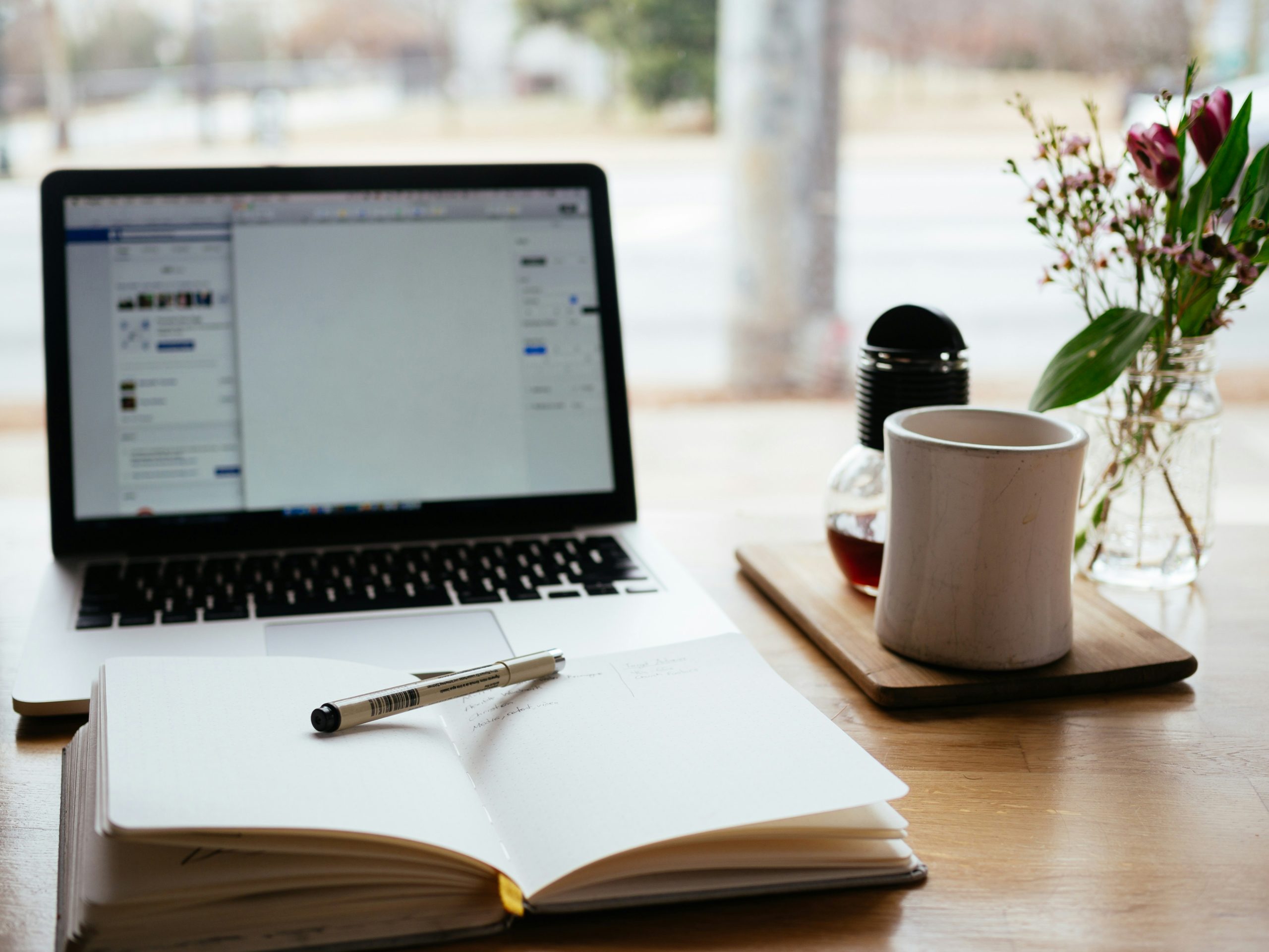 Laptop with paper and pen and a cup next to it.