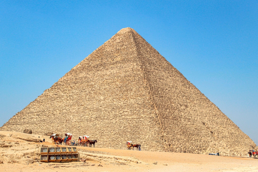 The iconic Great Pyramid of Giza stands tall under a clear blue sky, with tourists and camel riders at its base. fun facts about egypt
