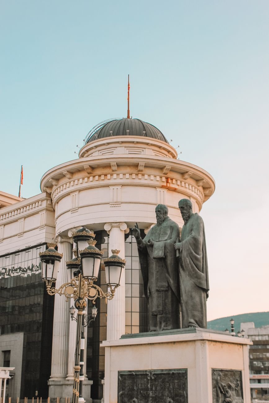 Statues stand near an ornamented building wall in a city square.
