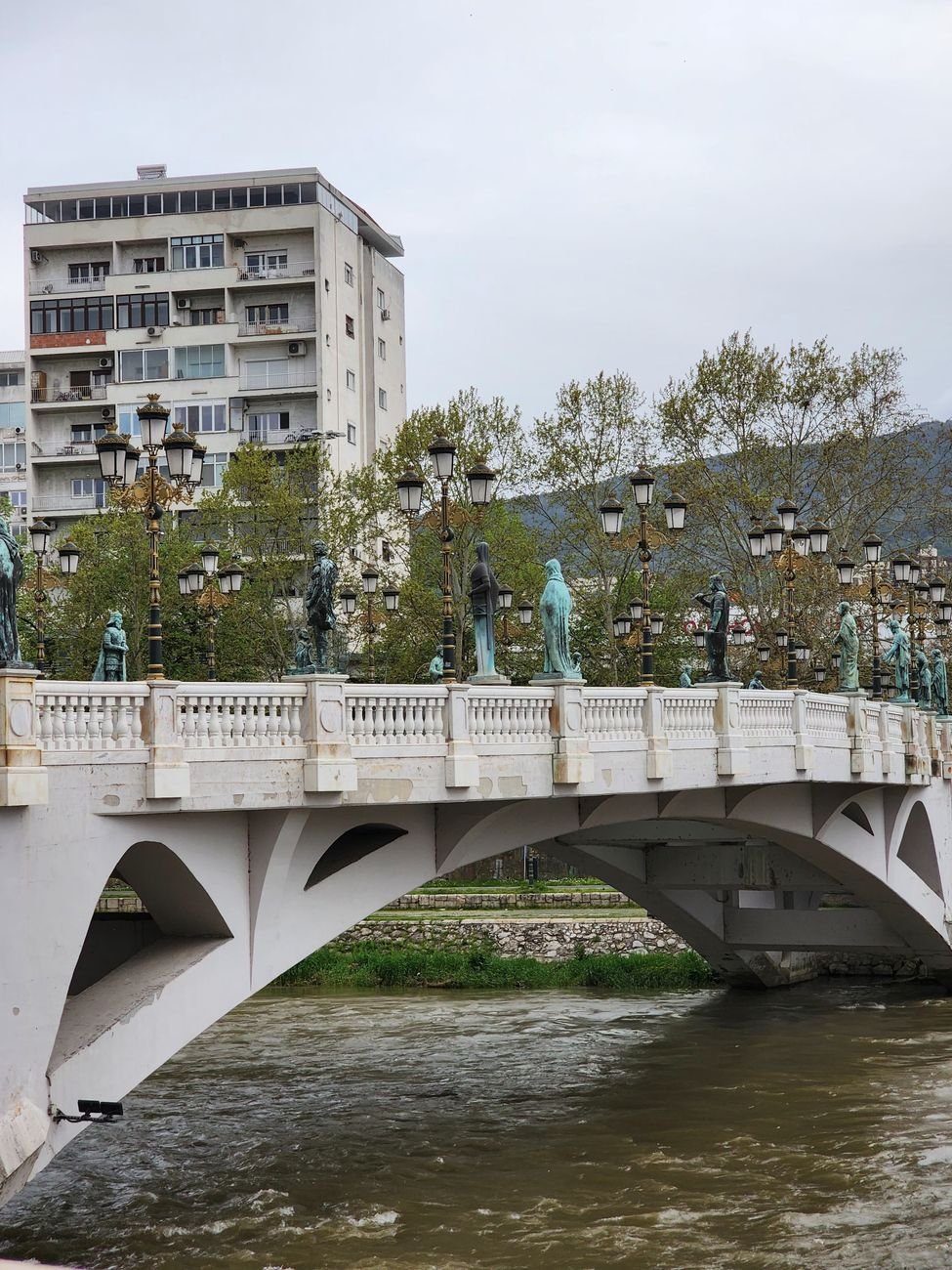 An ornamented pedestrian bridge over a river, lined with statues and lamp posts.