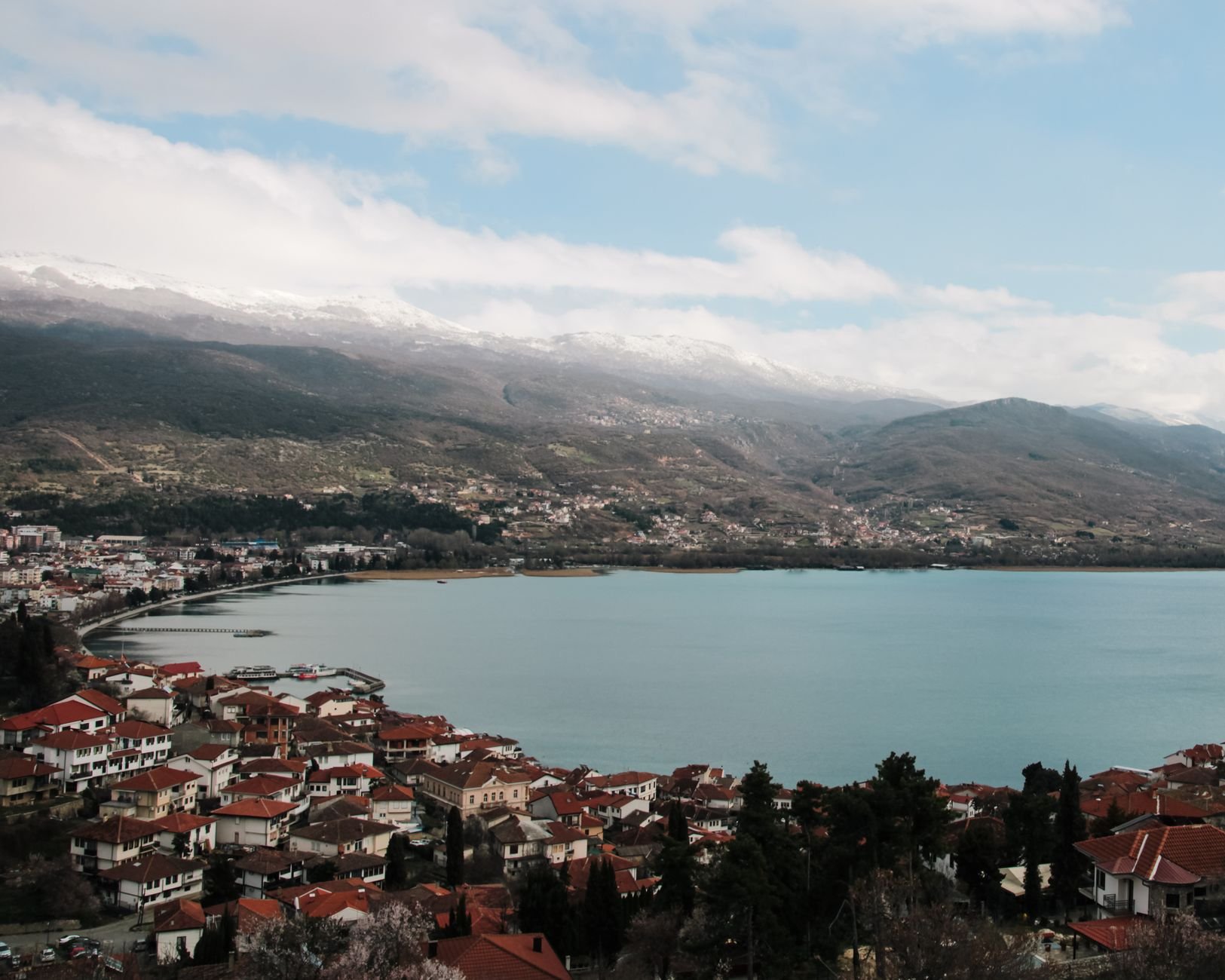 A wide lake framed by forested mountains under an open sky.