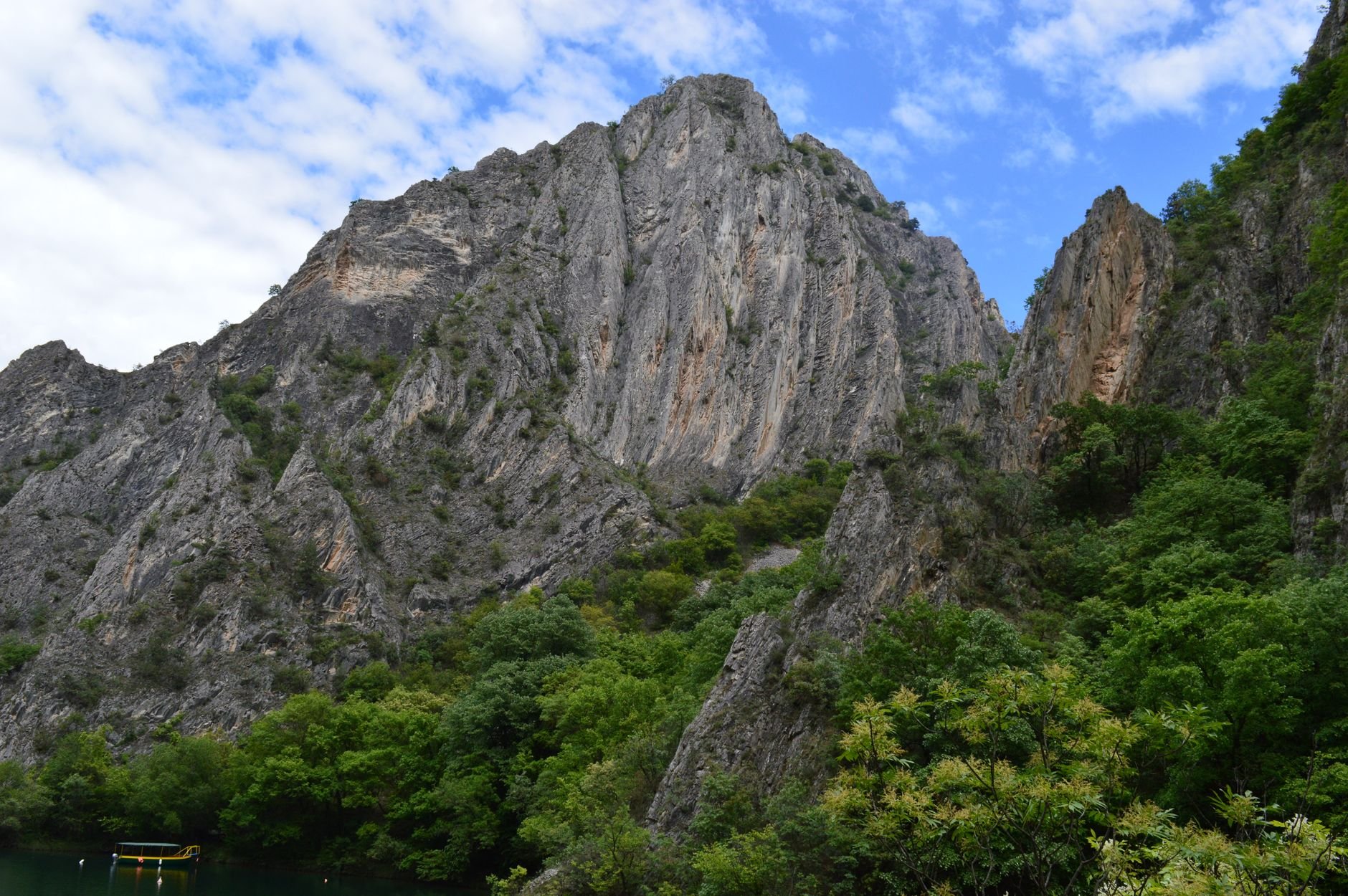 A steep rocky mountain rises directly above a narrow canyon lake.