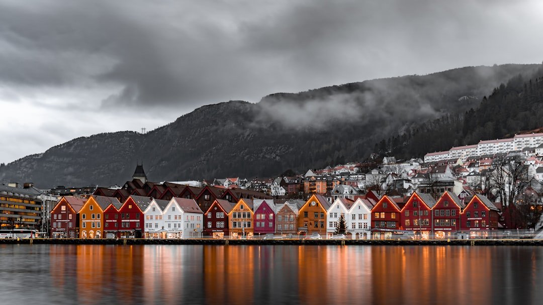 Mist drifts through a narrow fjord between steep mountain walls at dusk, with a small stone breakwater in the foreground.