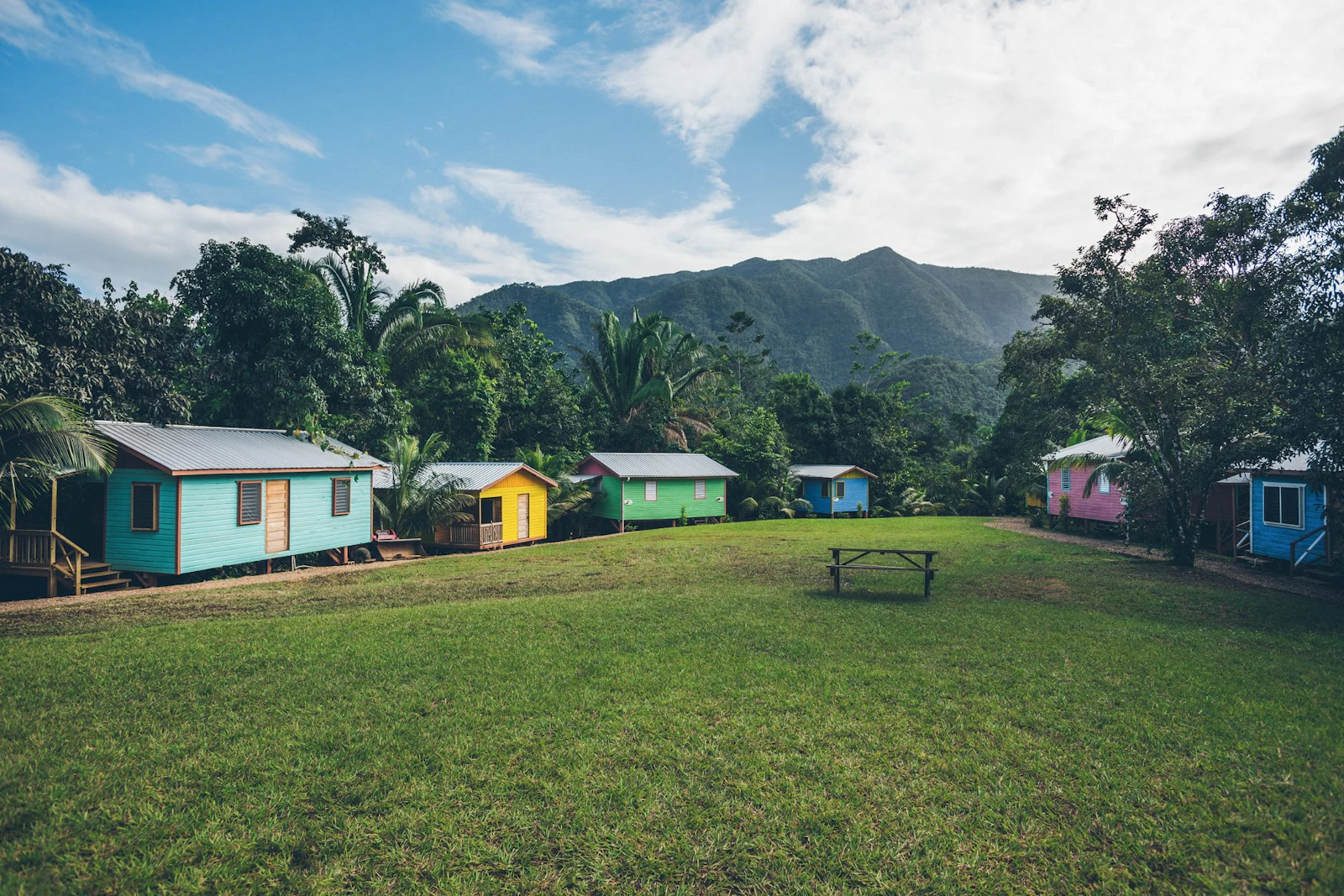 Colorful cabins line a grassy clearing below jungle-covered mountains in Belize