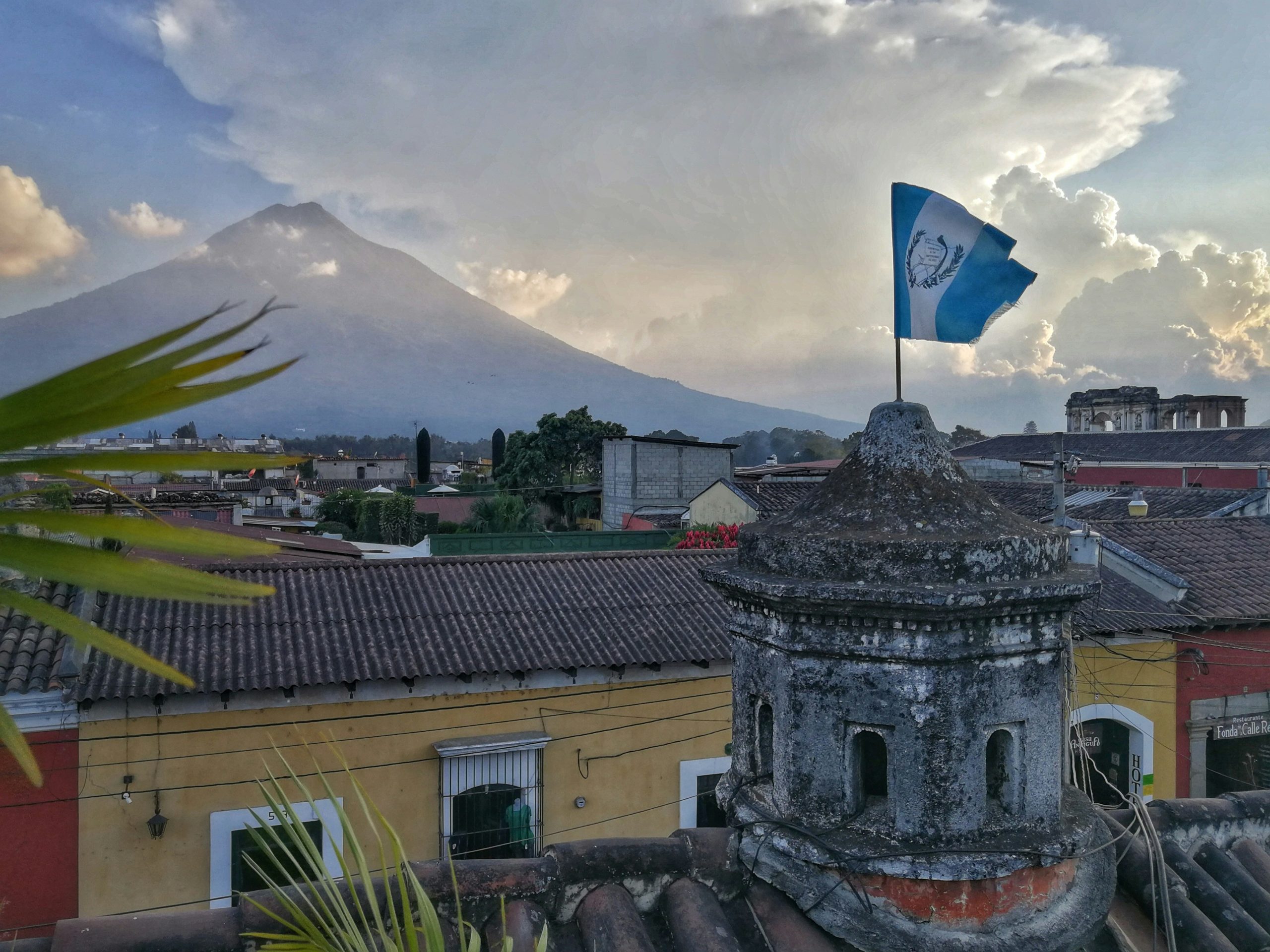 A national flag on a tiled rooftop at dusk, with a symmetrical volcanic cone rising over the low colonial town behind it.
