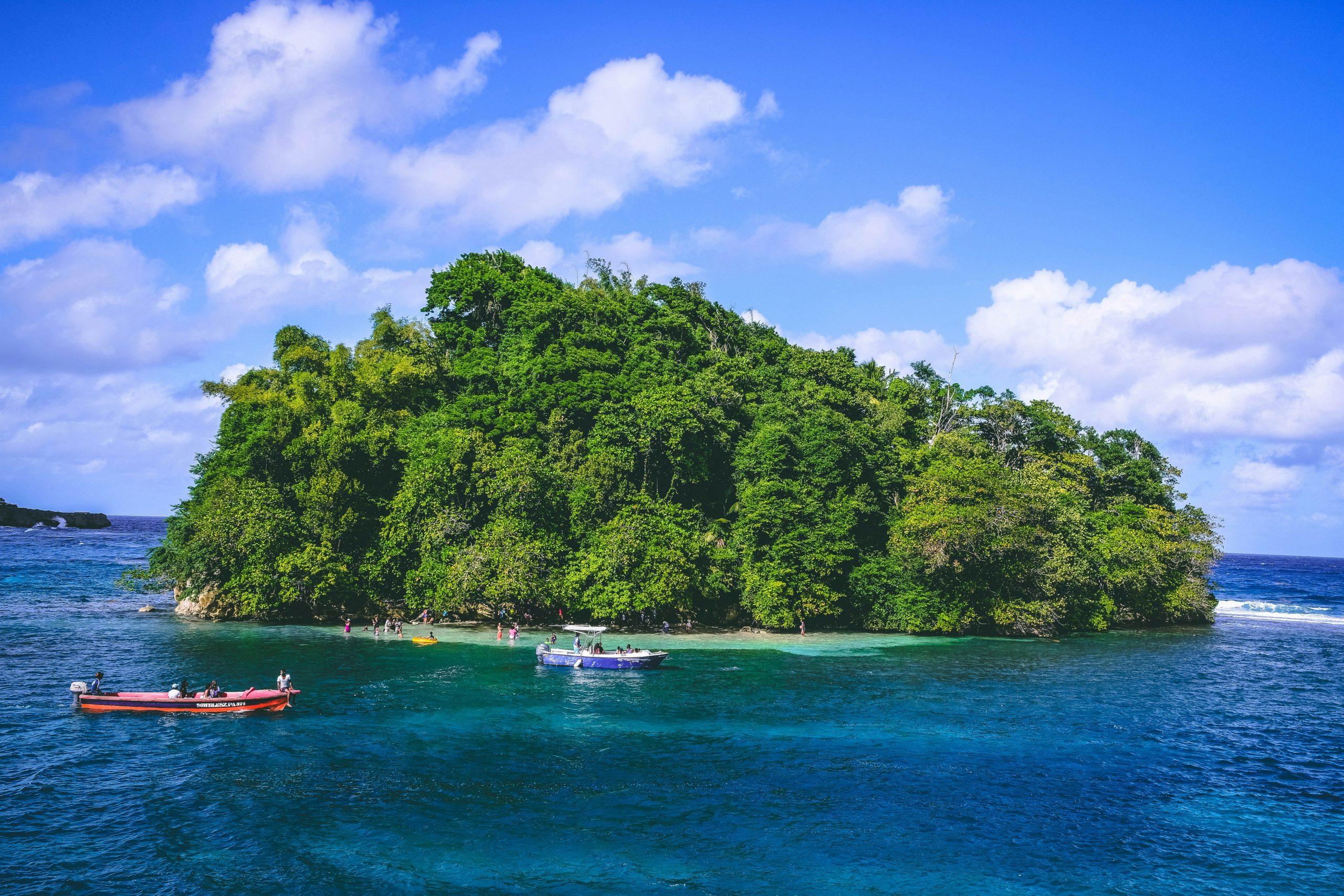Small lush green island in Jamaica surrounded by clear blue waters with boats nearby.