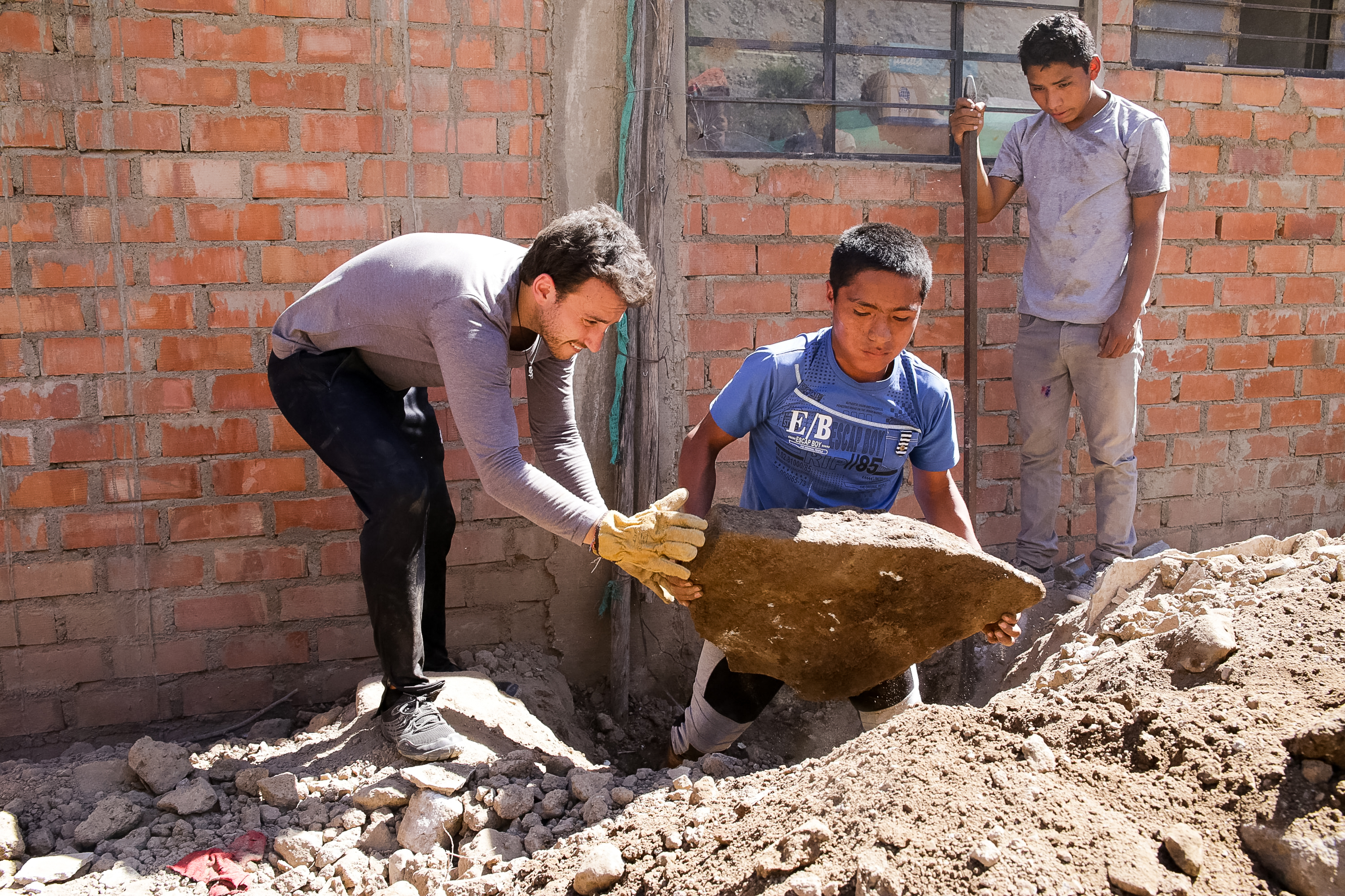 Teens lift a large rock together during a construction service project
