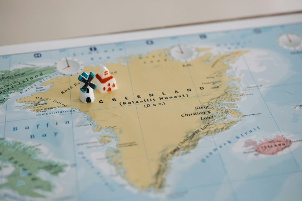 Photo by Lara Jameson: https://www.pexels.com/nb-no/bilde/retning-papir-kart-geografi-8828348/ Photo of Greenland on the map showing its relationship with Denmark with 2 small houses representing the 2 countries