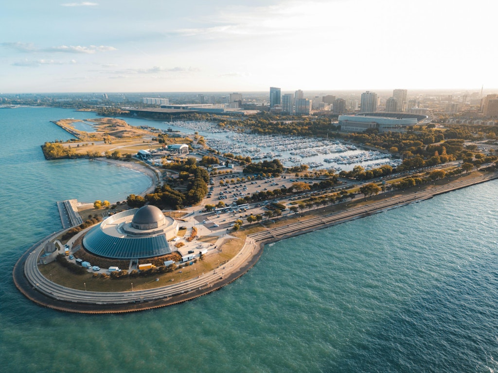Photo by Willian Justen de Vasconcellos: https://www.pexels.com/nb-no/bilde/luftfoto-av-moderne-bybilde-ved-innsjoen-28948282/ Shot of the Adler Planetarium against the lake.
