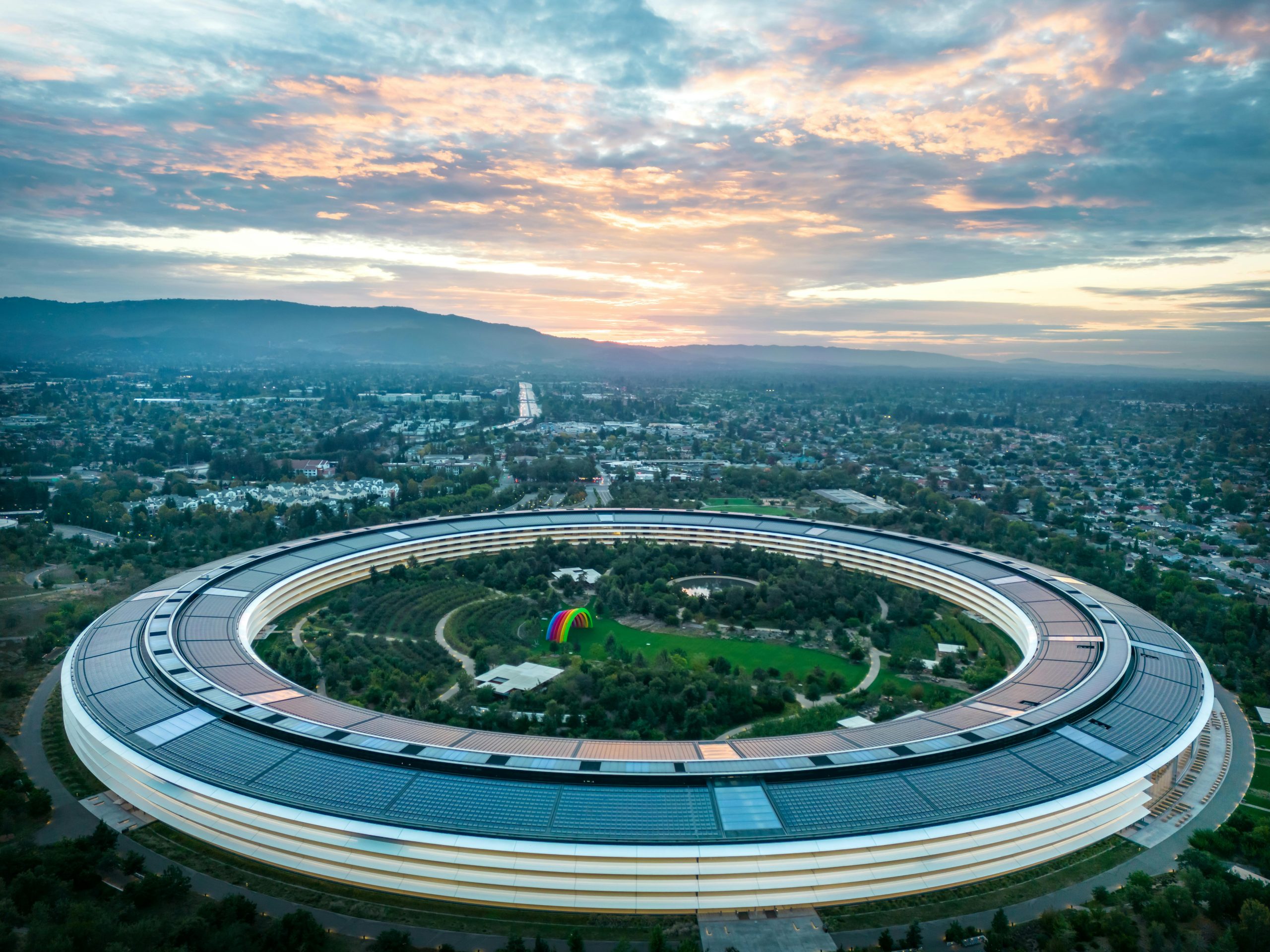 Aerial view of Apple's ring-shaped campus surrounded by green landscape at sunset