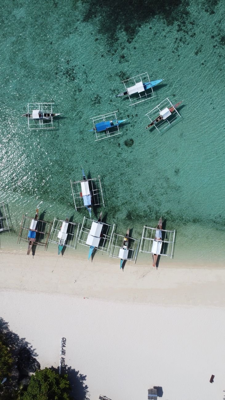 Wooden outrigger boats pulled up on a sandy beach.