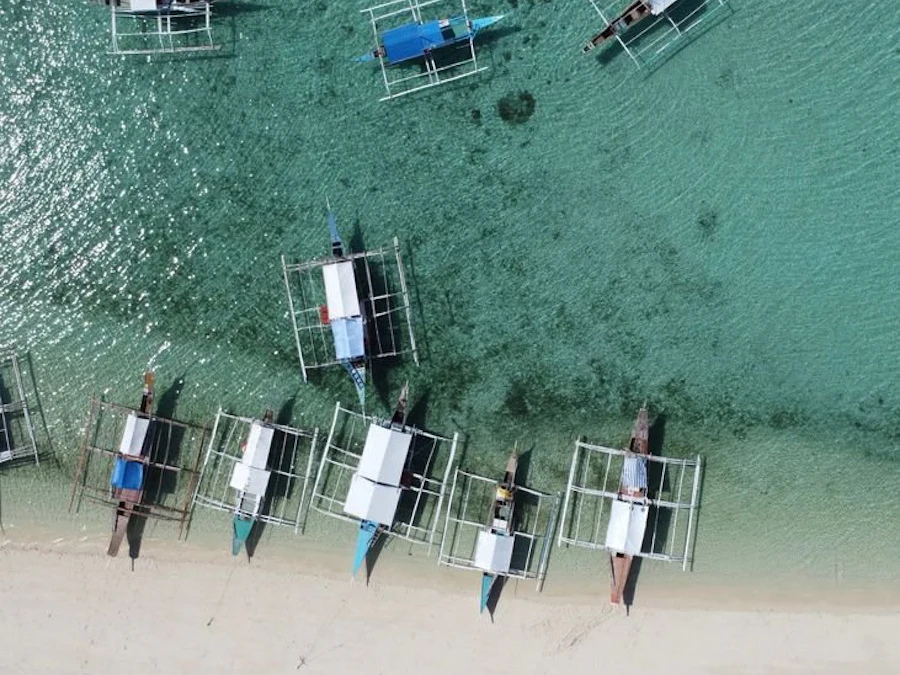 Wooden outrigger boats pulled up on a sandy beach.