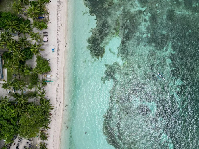 A curved white sand beach meeting turquoise water, seen from above.