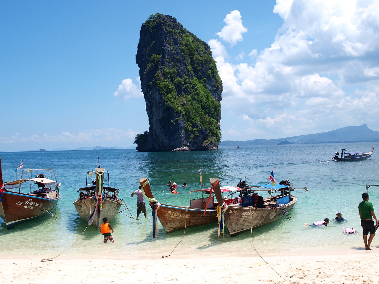 Longtail boats anchor near a limestone karst on a white-sand beach in Thailand