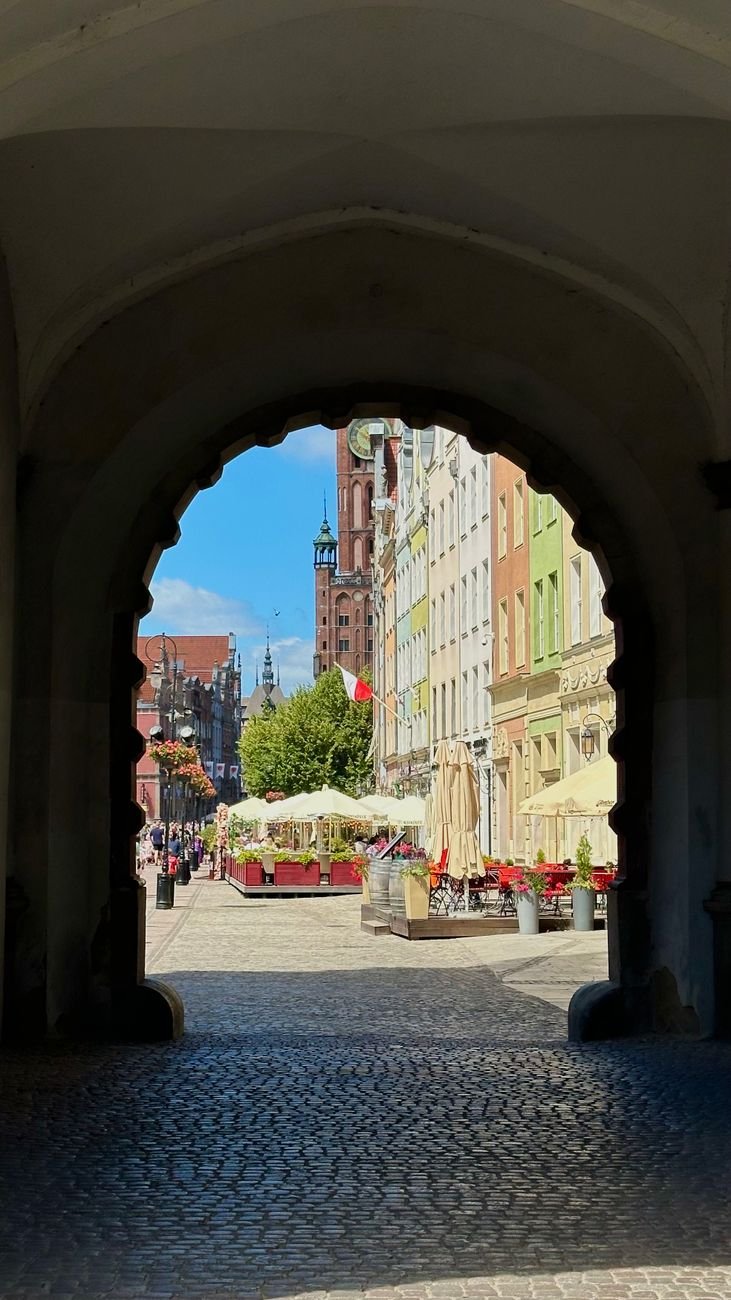 A view through a stone archway onto a colorful old town street lined with merchant houses.