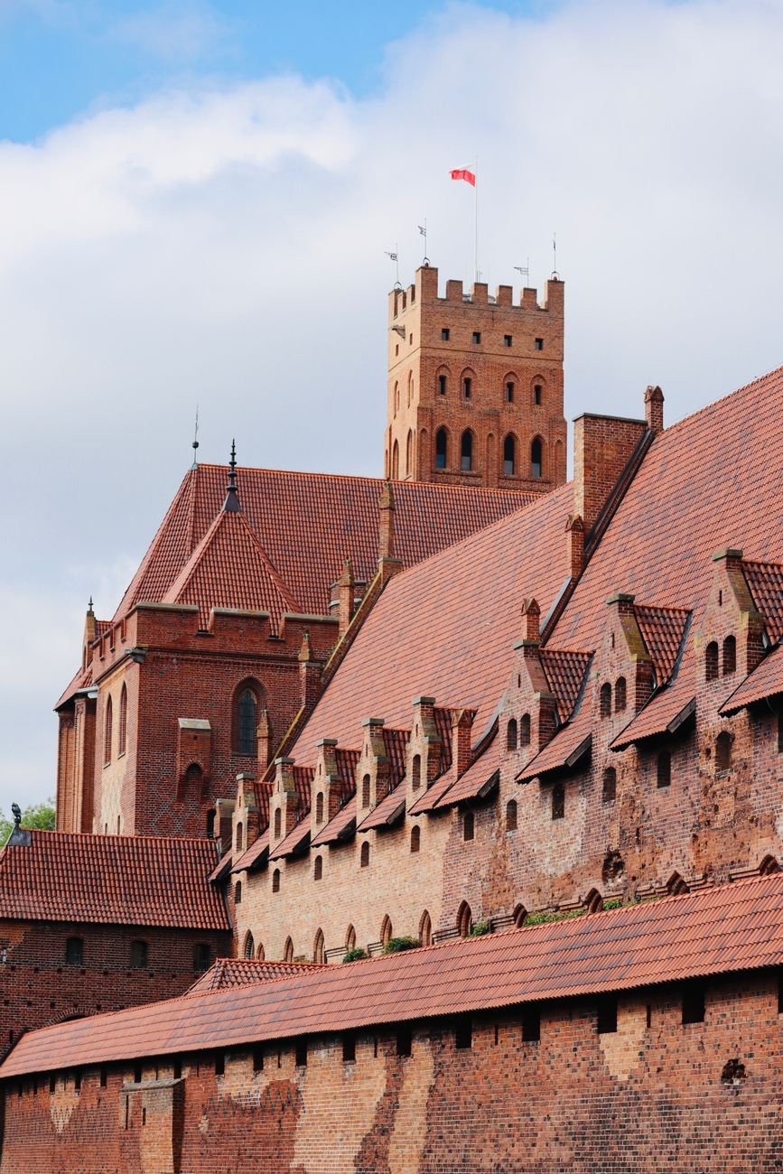 The red-brick towers and walls of a medieval castle above its moat.