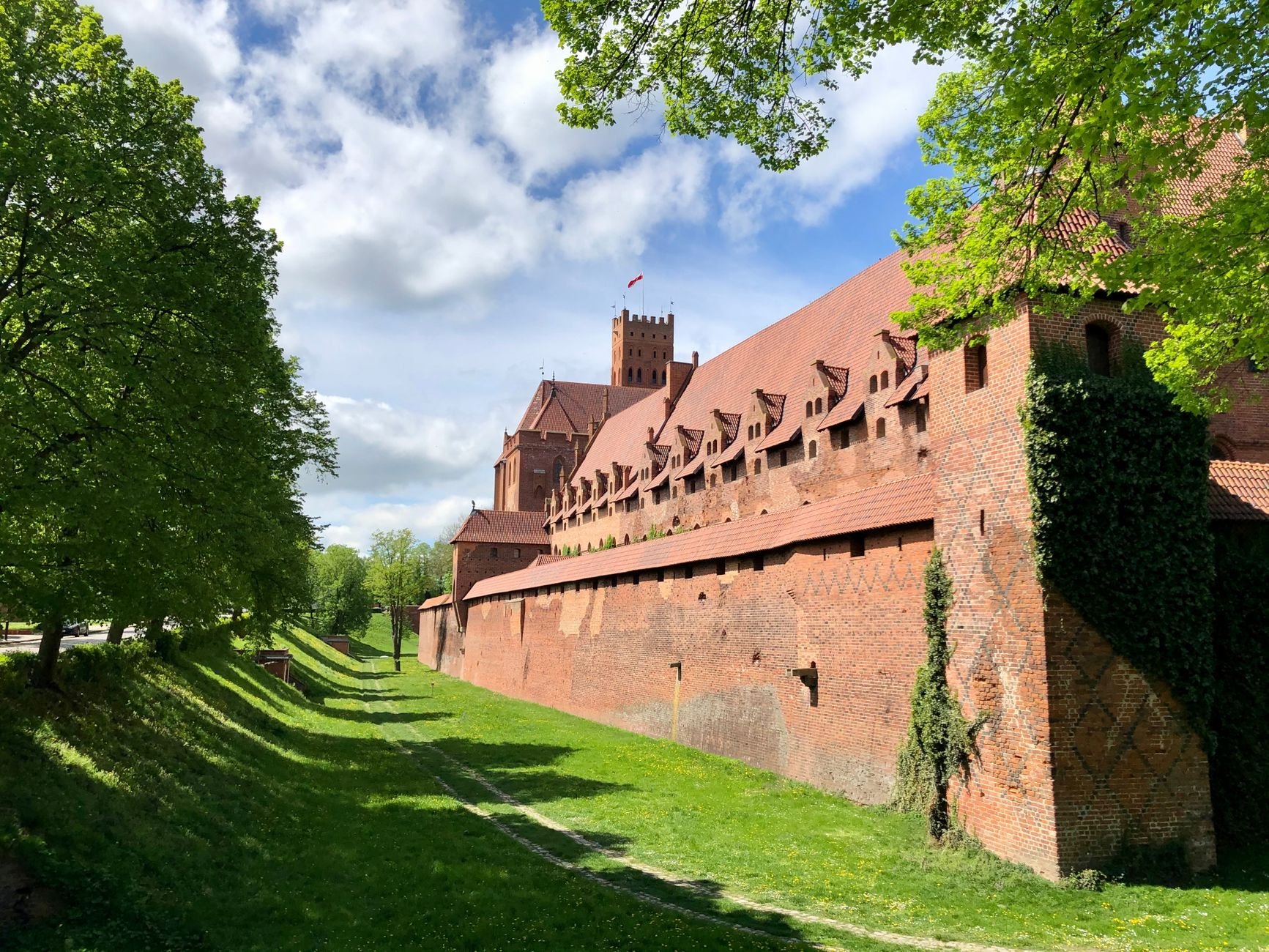 A medieval castle's brick ramparts reflected in the river beside it.