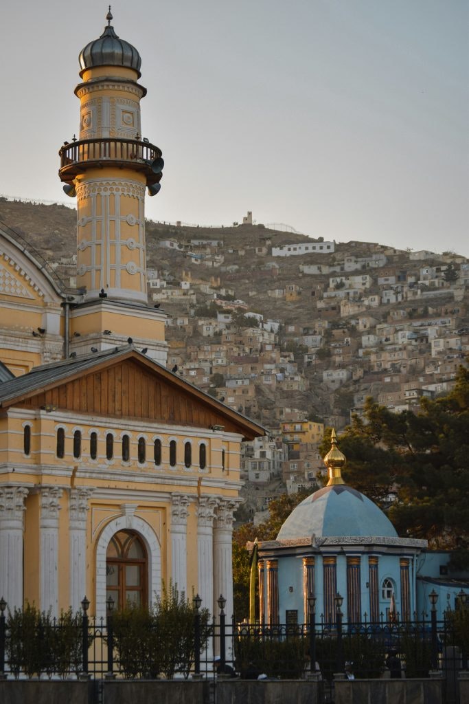 A historic mosque with a tall minaret, set against a hillside with homes.