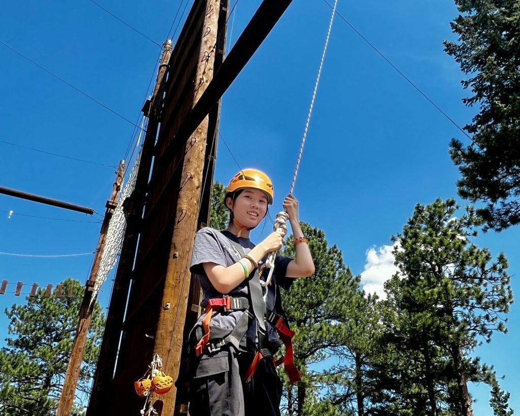 A student wearing a hardhat, strapped into a harness doing an outdoor obstacle course.
