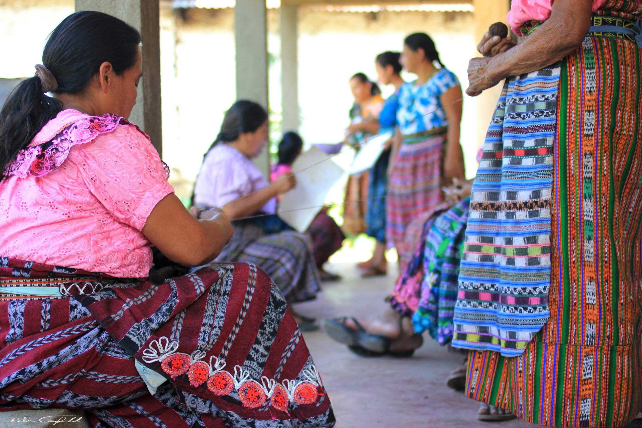 Teen travelers gather with women in traditional Mayan woven skirts and huipiles under a covered porch