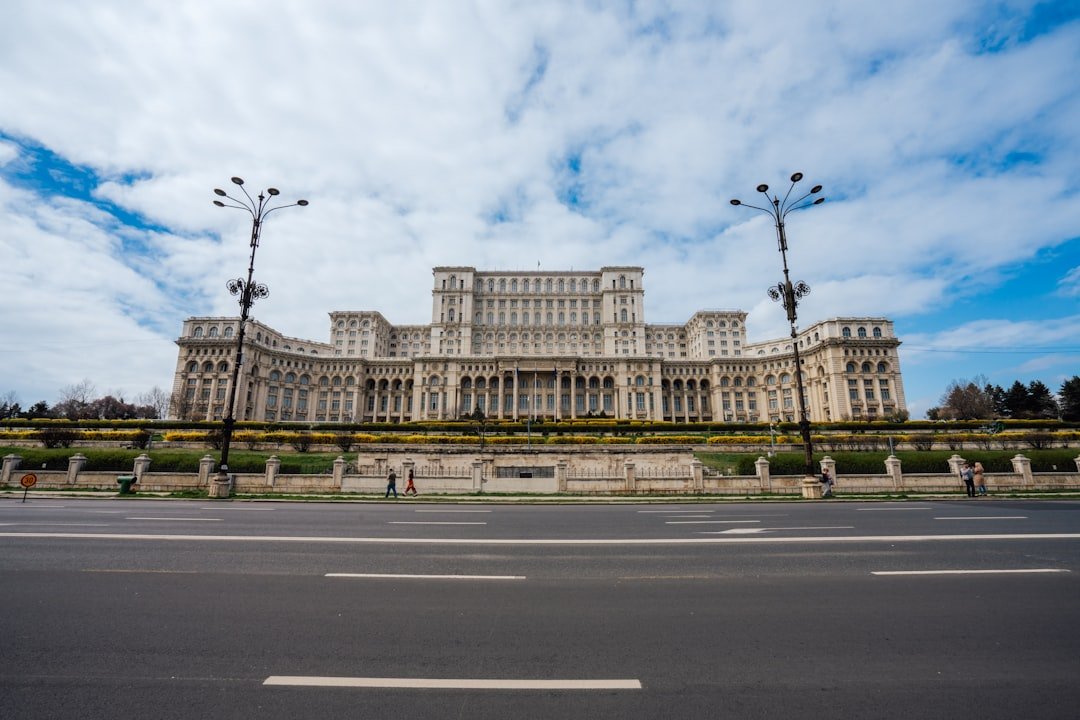 A large domed government building with rows of columns and arched windows stands beyond a wide boulevard lined with lamp posts.