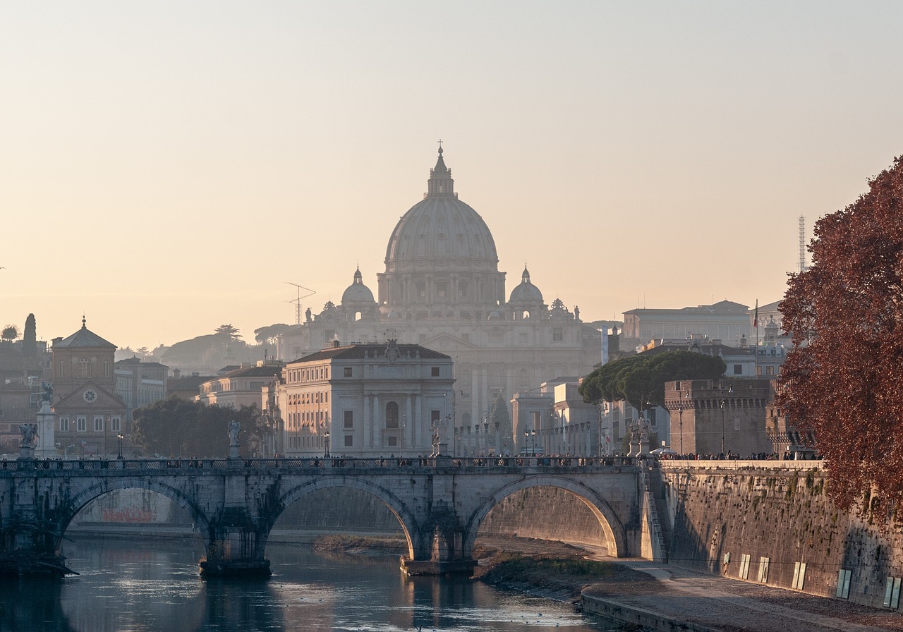 St. Peter's Basilica dome rises above the Tiber River and a stone bridge in Rome at dusk