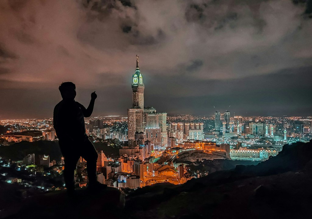 A man stands silhouetted against the nightscape of Makkah.