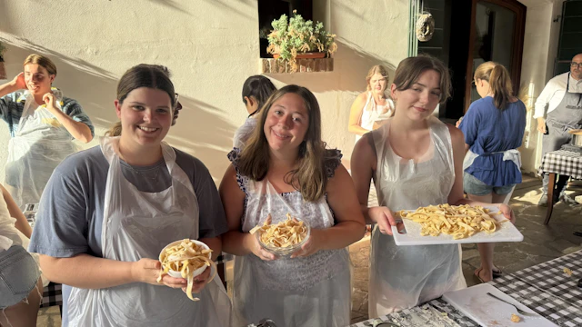 Three teen travelers in aprons hold bowls and a tray of fresh pasta they made in Italy