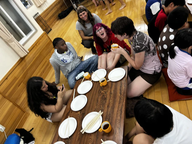 Students and hosts sit around plates of food on a wooden floor in Japan