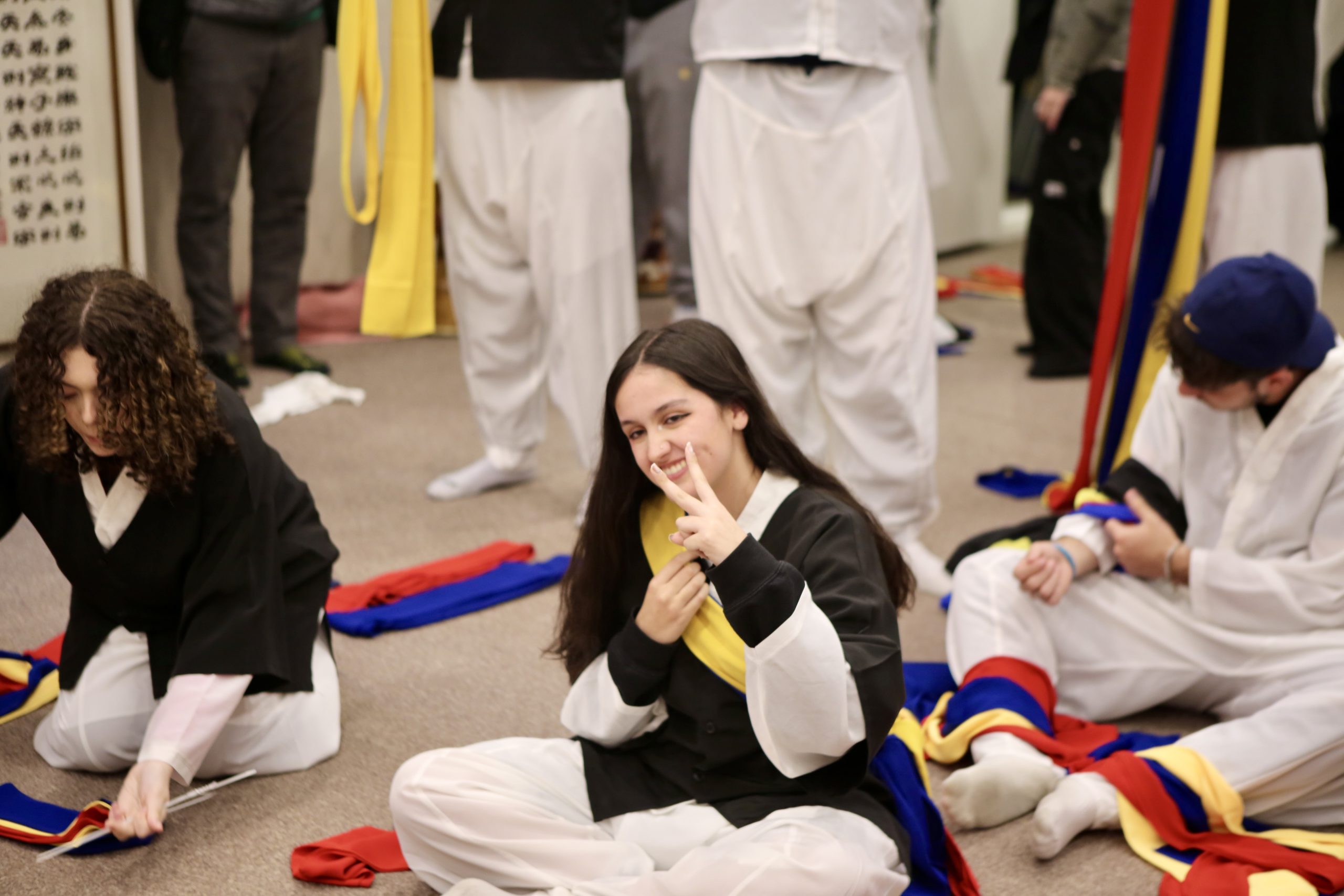 Students in traditional Korean dress sitting with performance sashes during a cultural workshop